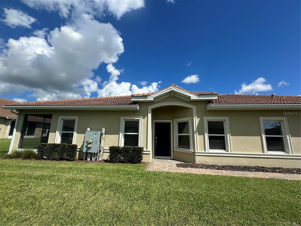 A single-story house with a tan stucco exterior, tile roof, and a paved walkway — 1068 QUAKER RIDGE LANE, DAVENPORT, FL