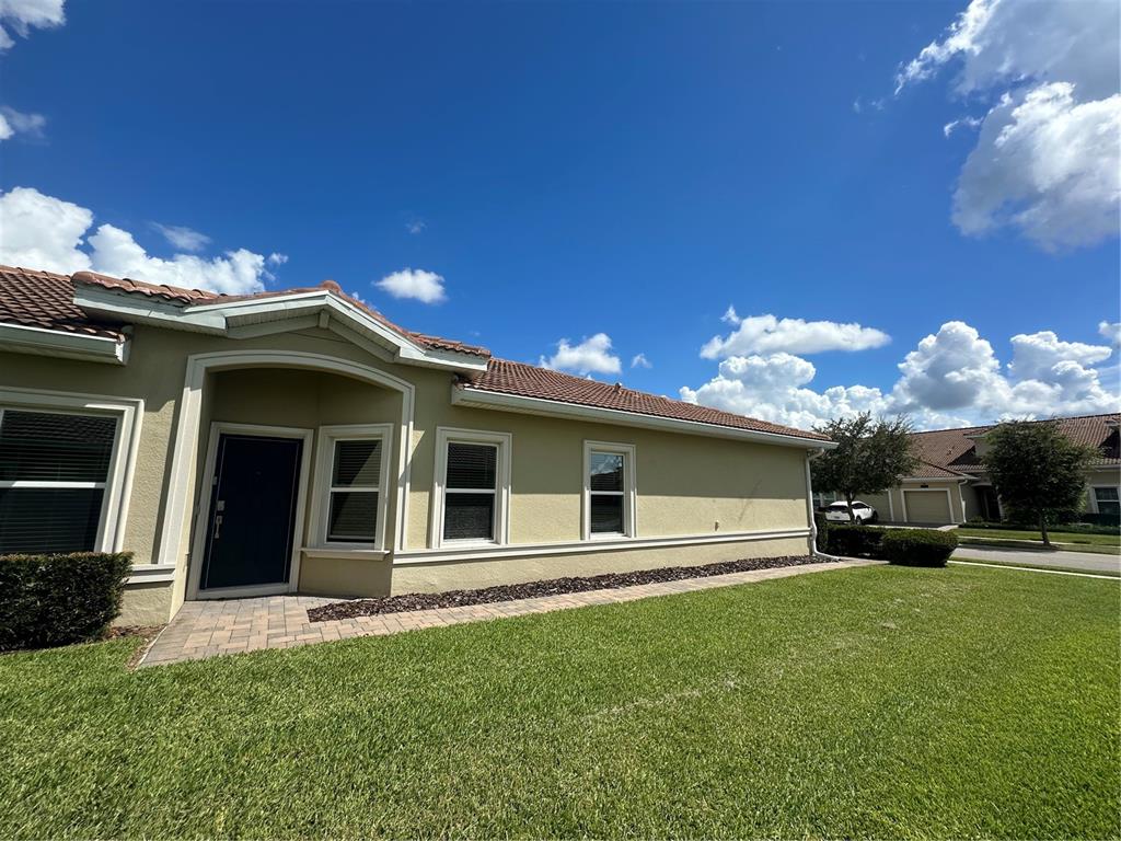 The exterior of a beige stucco house features a tiled roof and a paved walkway — 1068 QUAKER RIDGE LANE, DAVENPORT, FL