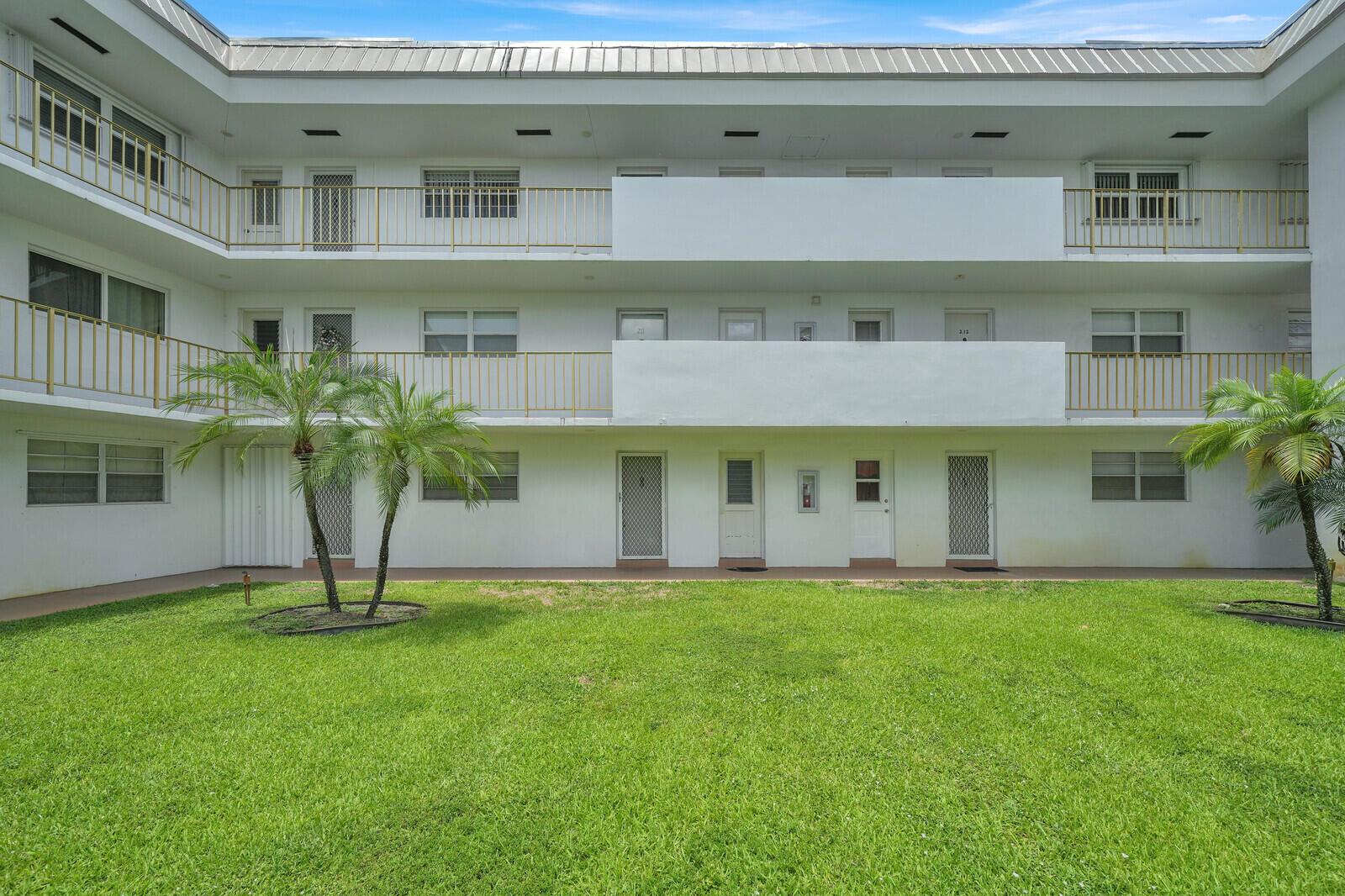 A three-story apartment building exterior features white walls, gold railings, and a grassy courtyard — 5501 NW 2nd Avenue # 111, Boca Raton FL 33487, BOCA RATON, FL