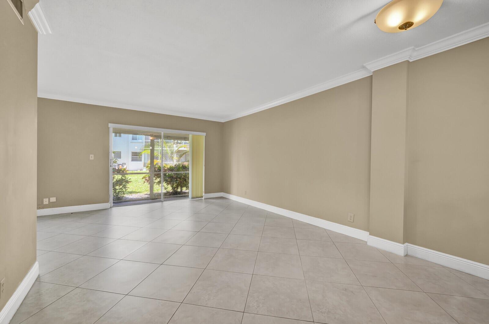 An empty living room features beige walls, white crown molding, and large light-colored floor tiles — 5501 NW 2nd Avenue # 111, Boca Raton FL 33487, BOCA RATON, FL