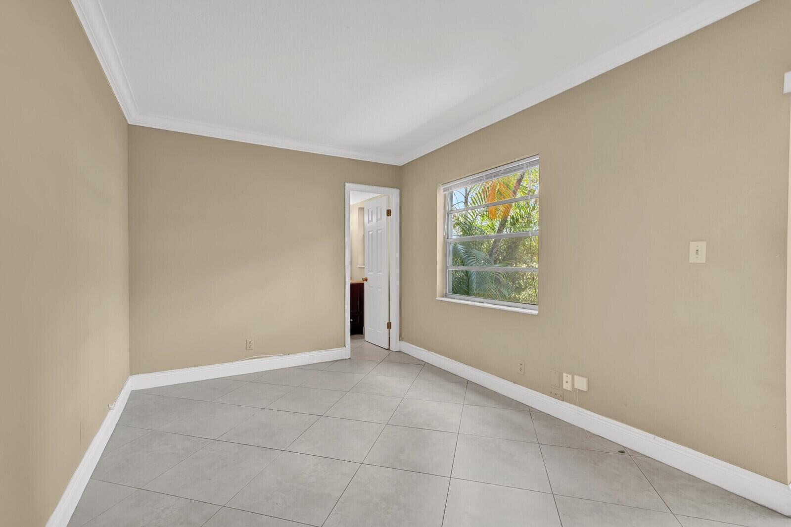 An empty room with beige walls, gray tile flooring, and a window overlooking palm trees — 5501 NW 2nd Avenue # 111, Boca Raton FL 33487, BOCA RATON, FL