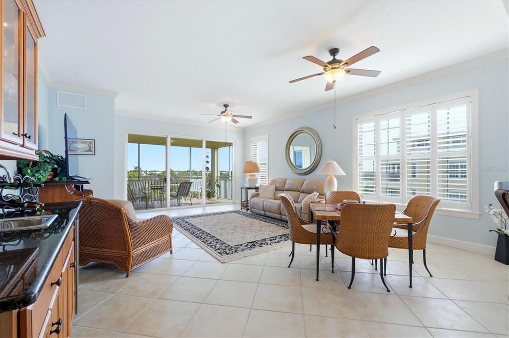 A bright living and dining area with tile floors, wicker furniture, and a balcony view — 8571 AMBERJACK CIRCLE UNIT 304, ENGLEWOOD, FL