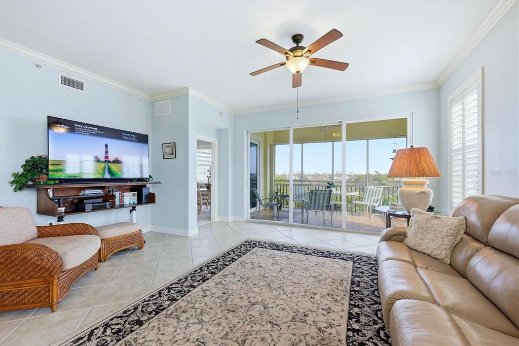 A living room features a television, a ceiling fan, tile floors, and a screened balcony — 8571 AMBERJACK CIRCLE UNIT 304, ENGLEWOOD, FL