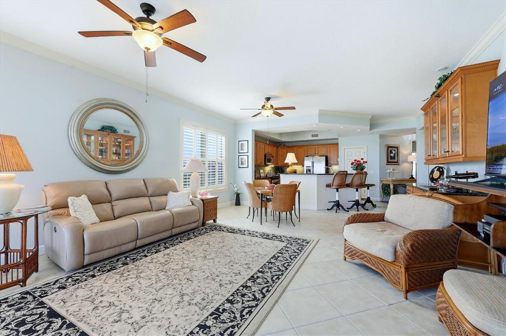 A living room and kitchen area with light tile floors, ceiling fans, and wicker furniture — 8571 AMBERJACK CIRCLE UNIT 304, ENGLEWOOD, FL