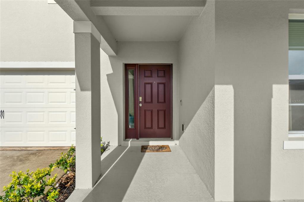 A covered entryway features a maroon front door with a side window and concrete flooring — 9649 BLACK WALNUT DRIVE, CLERMONT, FL