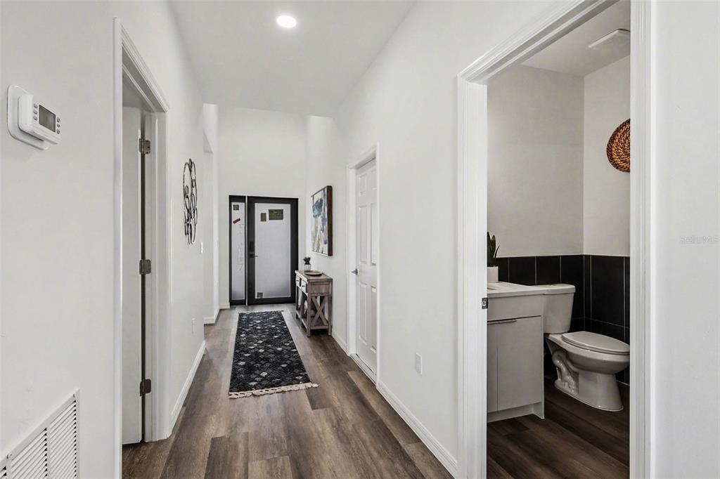 A hallway with wood-look flooring leads to an entryway, featuring a bathroom on the right — 1727 NE 12TH TERRACE, CAPE CORAL, FL