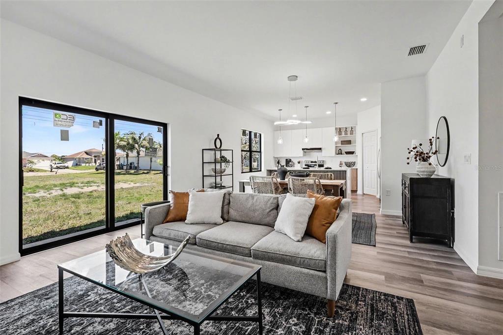 A living room with a grey sofa, glass coffee table, and open kitchen in the background — 1727 NE 12TH TERRACE, CAPE CORAL, FL