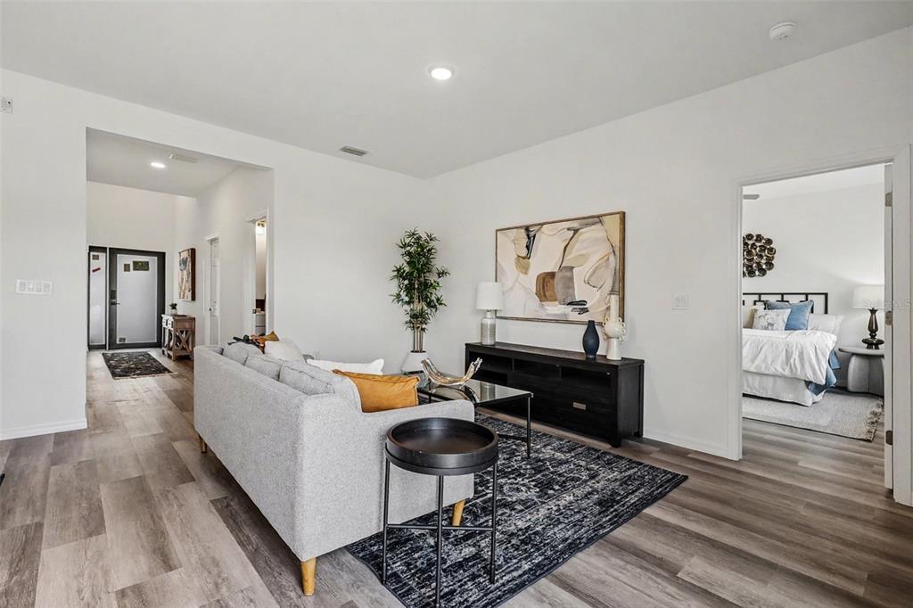 A living room with gray flooring, a sofa, a black media console, and an adjacent bedroom — 1727 NE 12TH TERRACE, CAPE CORAL, FL