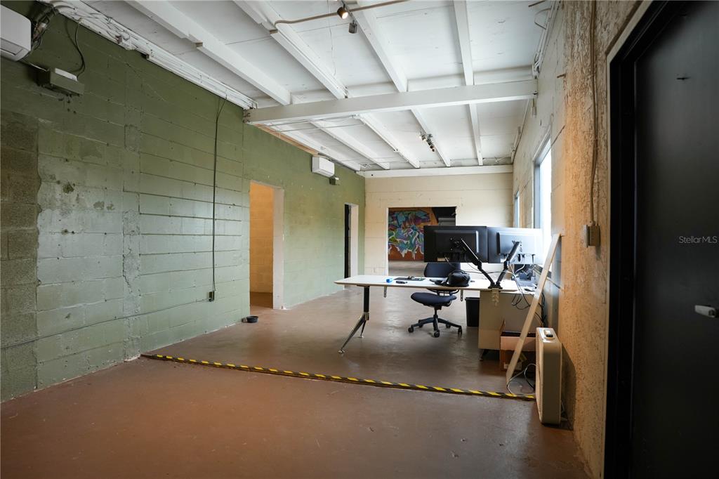 An industrial-style office space features a green concrete block wall, exposed ceiling beams, and a desk — 4700 22ND AVENUE S UNIT 3, ST PETERSBURG, FL