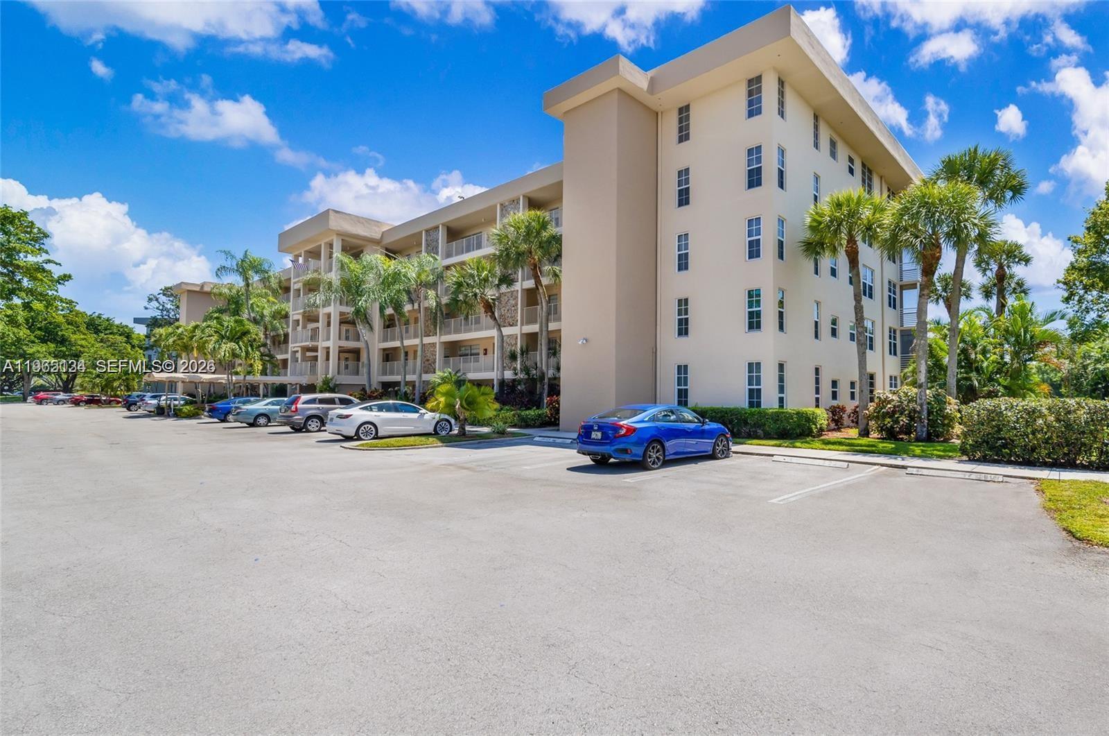 A multi-story apartment building with a parking lot in the foreground under a blue sky — 4030 W Palm Aire Dr # 104, Pompano Beach FL 33069, POMPANO BEACH, FL