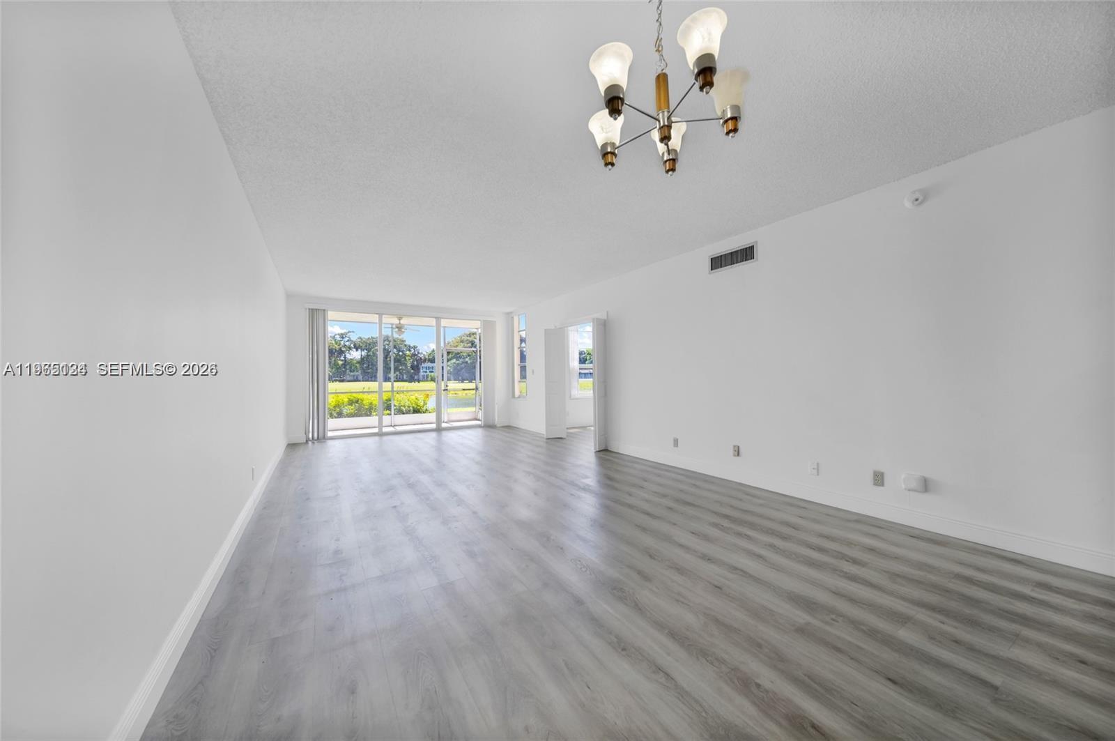 An empty living room features white walls, light gray wood-look flooring, and a sliding glass door — 4030 W Palm Aire Dr # 104, Pompano Beach FL 33069, POMPANO BEACH, FL