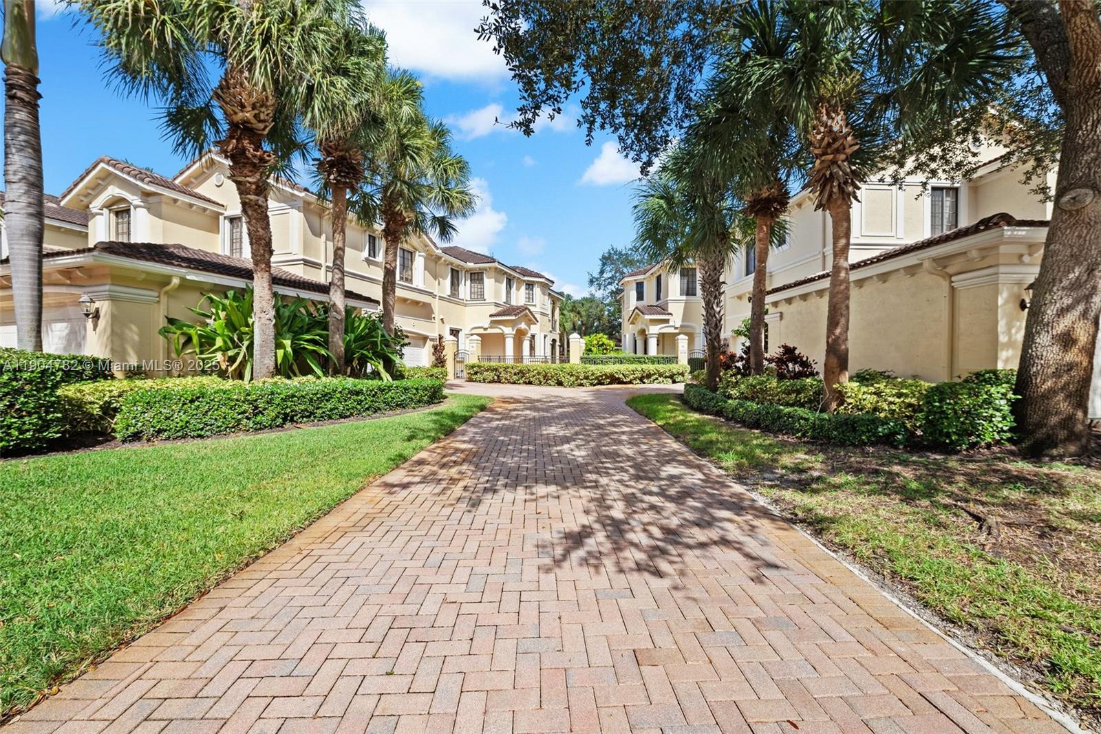 A brick driveway leads between two multi-story residential buildings surrounded by palm trees and landscaping — 1634 Passion Vine Cir # 2, Weston FL 33326, WESTON, FL