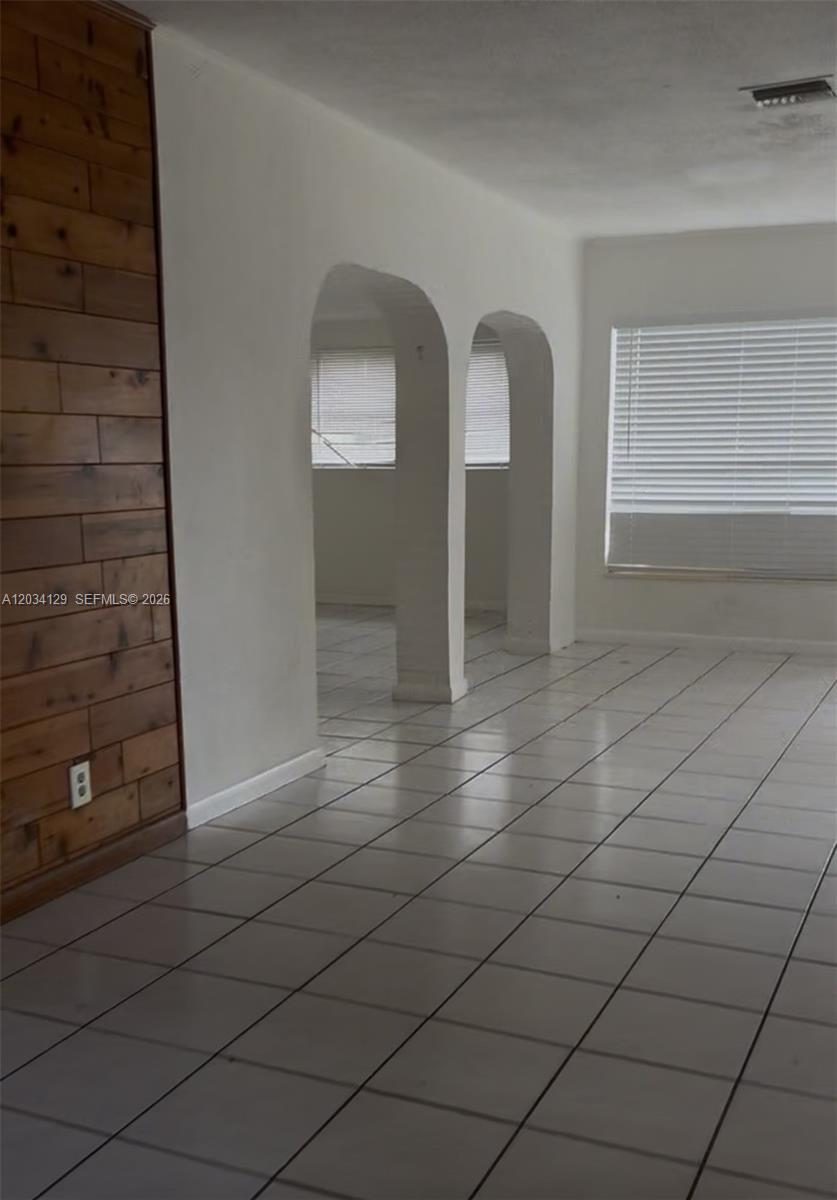 A room with white tiled floors, a wood-paneled accent wall, and two arched doorways — 6732 Atlanta St, Hollywood FL 33024, HOLLYWOOD, FL