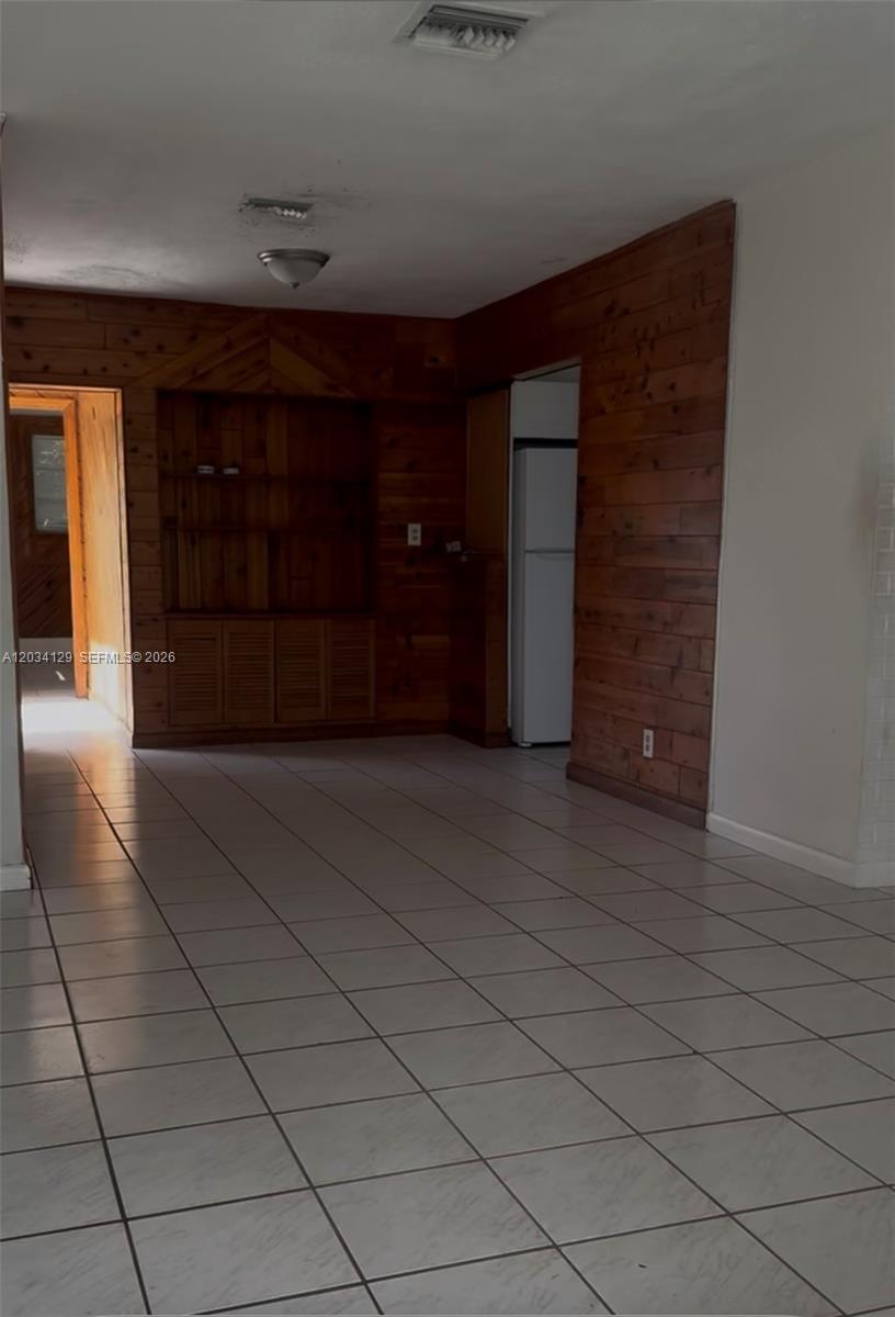 A room with light-colored tile flooring and wood-paneled walls featuring a built-in shelving unit — 6732 Atlanta St, Hollywood FL 33024, HOLLYWOOD, FL