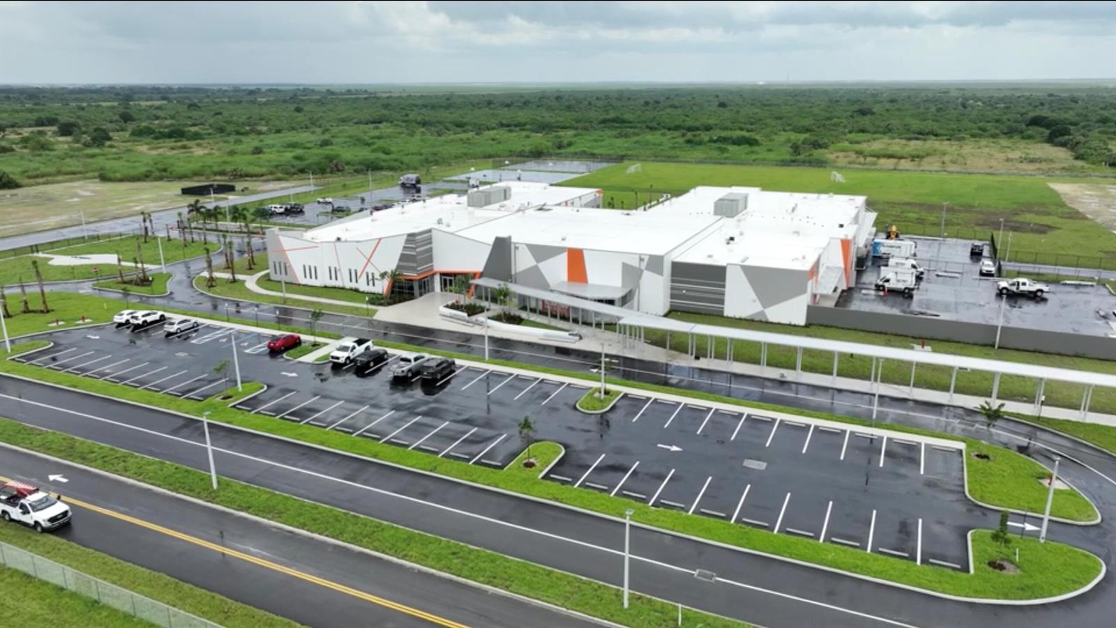 An aerial view shows a modern school building with a parking lot and surrounding fields — 13663 SW Vine Drive, FL 34956, FL