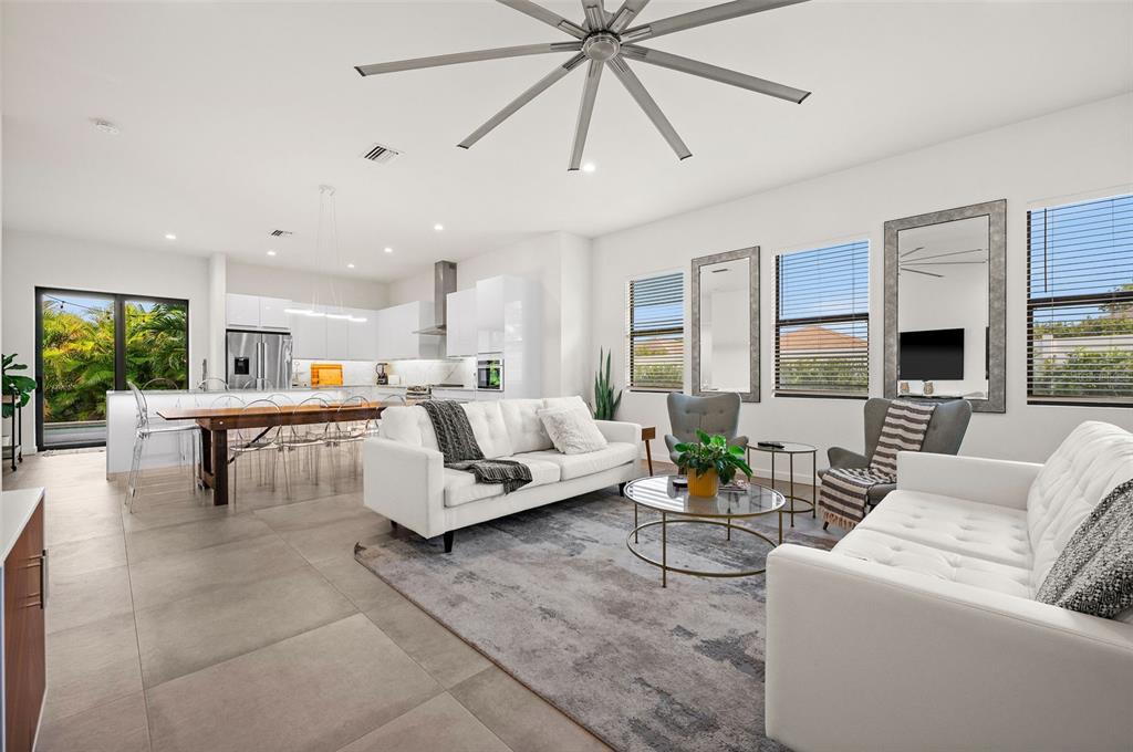 A modern open-concept living room and kitchen featuring white sofas, tile floors, and large windows — 5351 MOELLER AVENUE, SARASOTA, FL