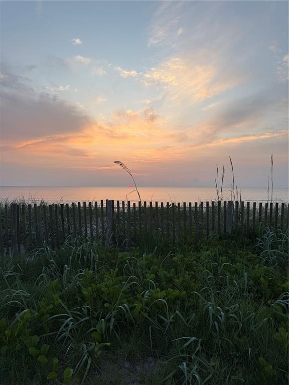 A wooden fence separates grassy dunes from a calm ocean under a sunset sky — 38 SQUASH BLOSSOM TRAIL, PALM COAST, FL