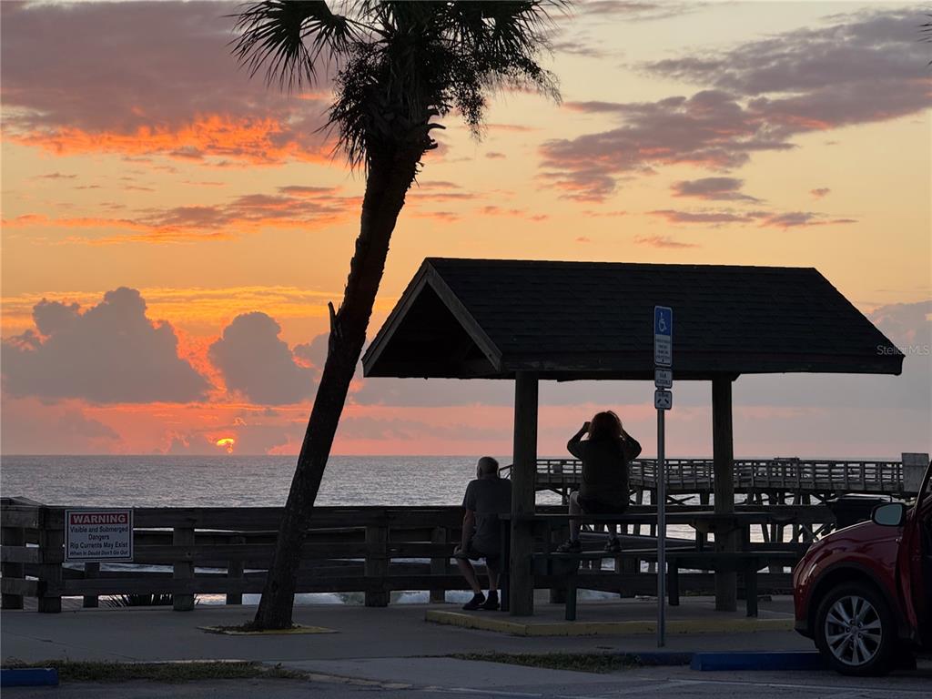 A couple sits at a picnic table under a pavilion overlooking the ocean at sunset — 38 SQUASH BLOSSOM TRAIL, PALM COAST, FL