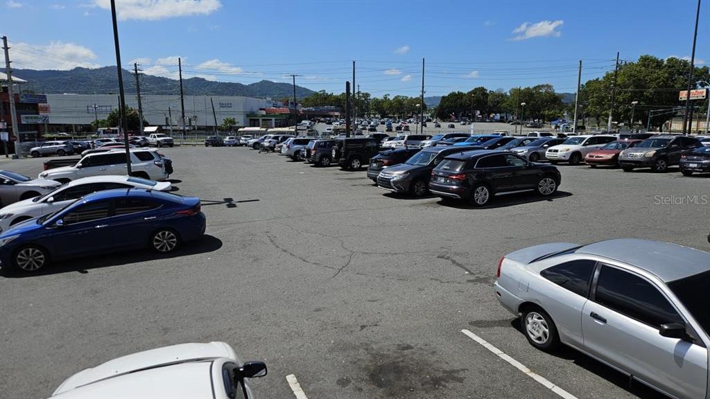 A large, paved outdoor parking lot filled with many parked cars under a blue sky — PR-1 INT. SAN CARLOS ST., CAGUAS, PR