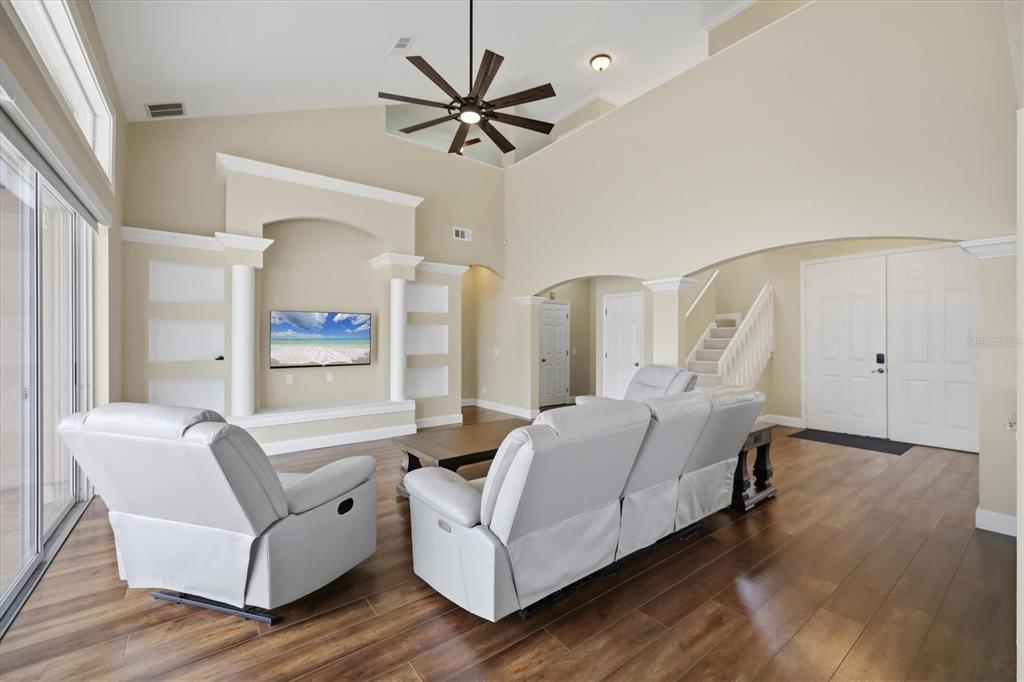 A living room features a vaulted ceiling, a wall-mounted television, and light-colored leather furniture — 4907 50TH AVENUE W, BRADENTON, FL