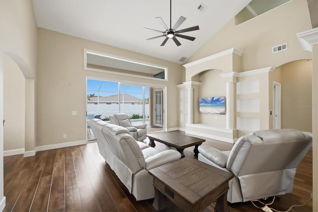 A living room features a vaulted ceiling, wood flooring, a built-in media wall, and sliding doors — 4907 50TH AVENUE W, BRADENTON, FL