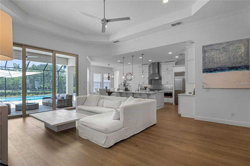 A bright open-concept living room features a white sectional, hardwood floors, and a kitchen view — 1118 ESTANCIA WOODS LOOP, WINDERMERE, FL