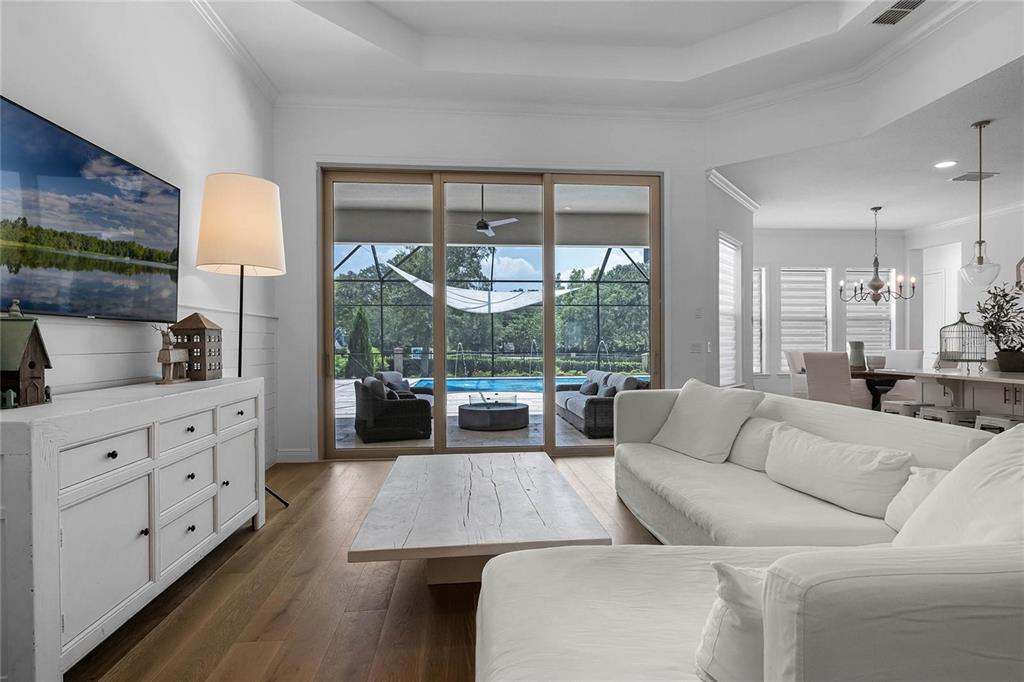 A living room with white furniture, wood floors, and sliding doors opening to a pool — 1118 ESTANCIA WOODS LOOP, WINDERMERE, FL
