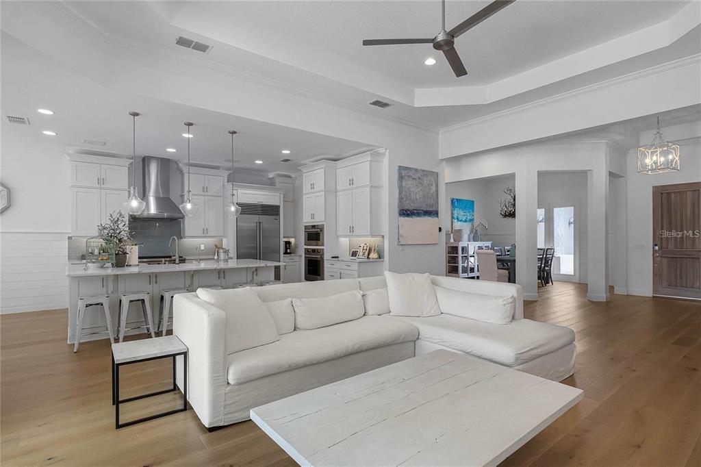 A bright open-concept living room and kitchen featuring white cabinetry, light wood floors, and furniture — 1118 ESTANCIA WOODS LOOP, WINDERMERE, FL