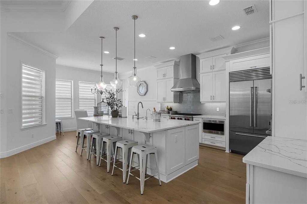 A modern white kitchen features a large marble-topped island, stainless steel appliances, and wood flooring — 1118 ESTANCIA WOODS LOOP, WINDERMERE, FL