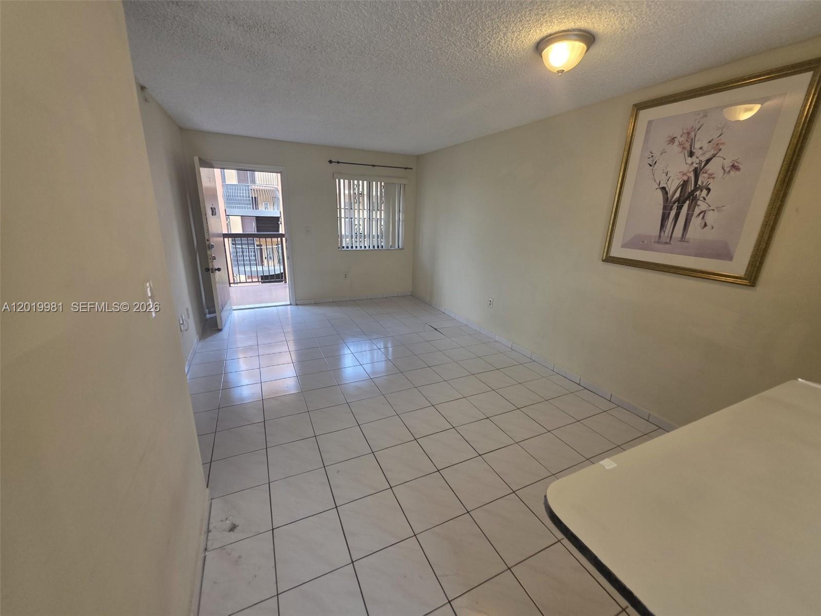 An empty room features white tile flooring, a ceiling light, and an open exterior door — 5500 W 21st Ct # 306, Hialeah FL 33016, HIALEAH, FL