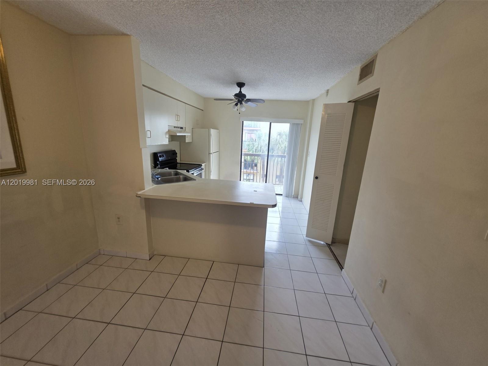 A kitchen with white cabinets and a breakfast bar opens to a balcony — 5500 W 21st Ct # 306, Hialeah FL 33016, HIALEAH, FL