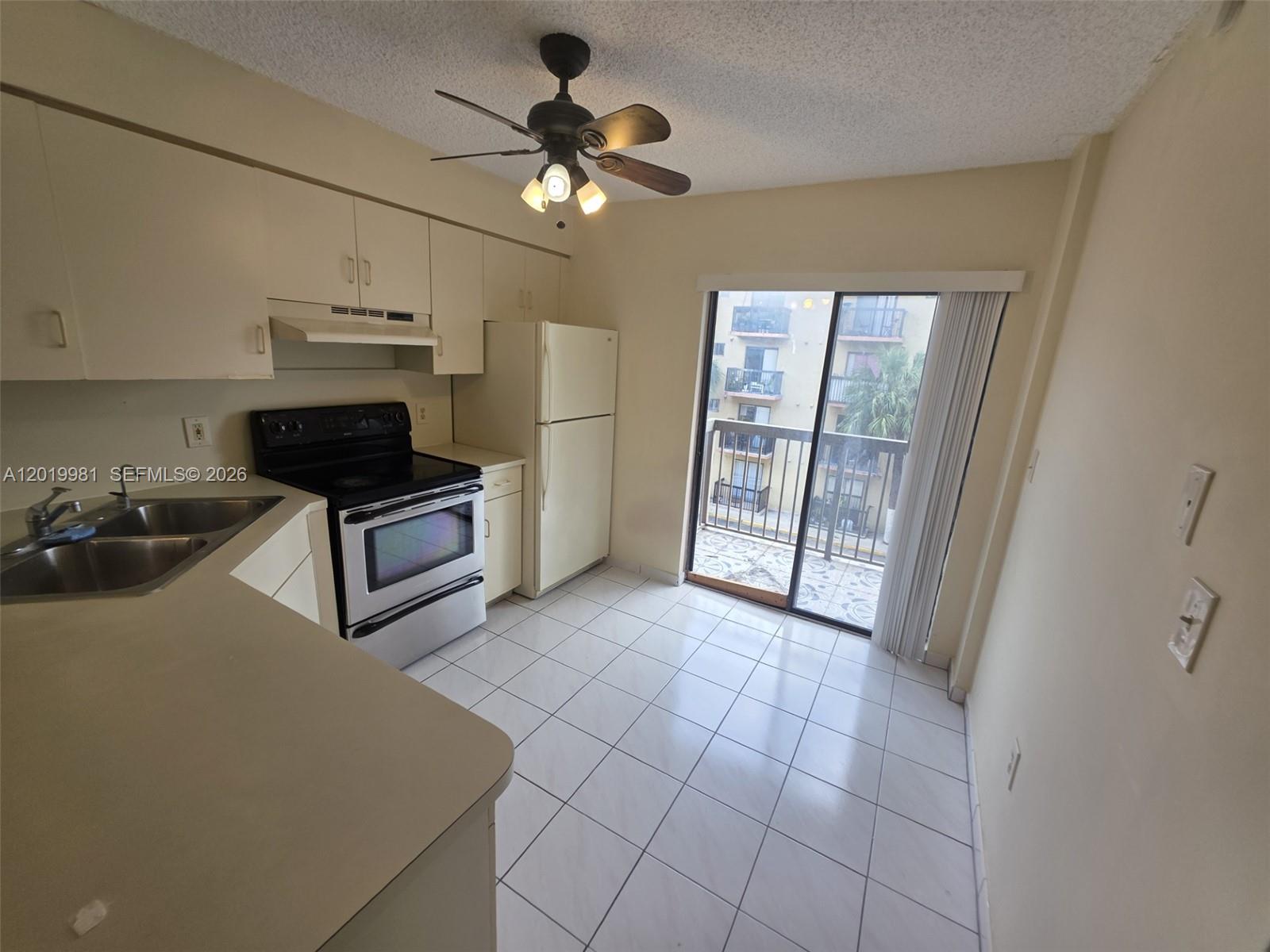 This kitchen features white tile floors, light-colored cabinetry, a ceiling fan, and a sliding door — 5500 W 21st Ct # 306, Hialeah FL 33016, HIALEAH, FL