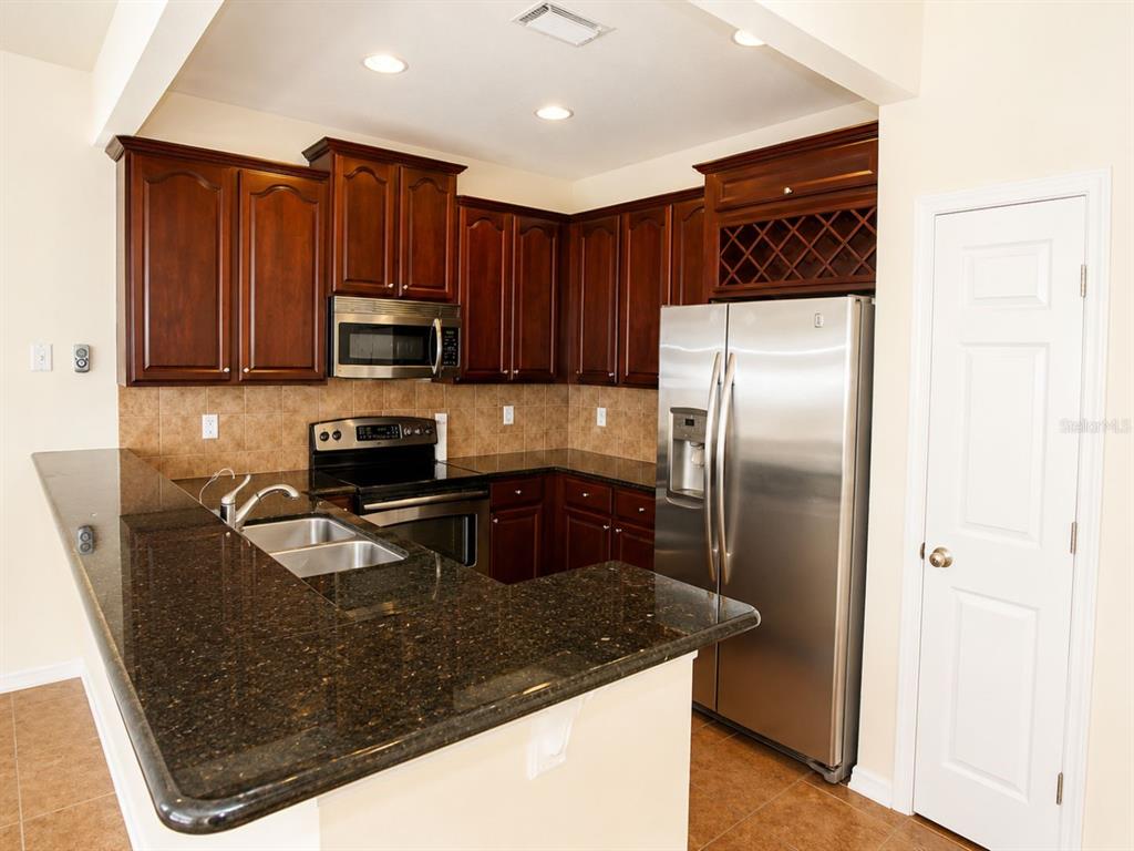 A kitchen with dark wood cabinets, granite countertops, stainless steel appliances, and tile flooring — 1515 BOWMORE DRIVE, CLEARWATER, FL