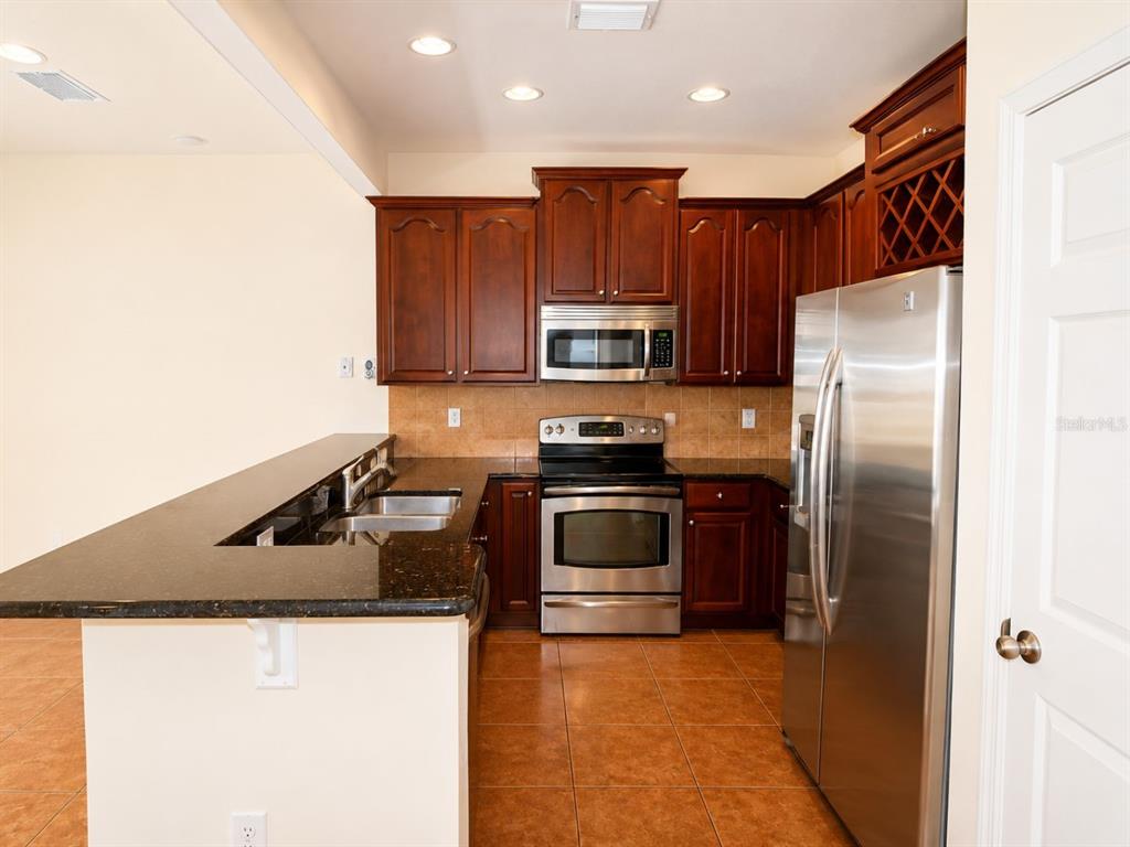 A kitchen features dark wood cabinets, stainless steel appliances, granite countertops, and tiled flooring — 1515 BOWMORE DRIVE, CLEARWATER, FL