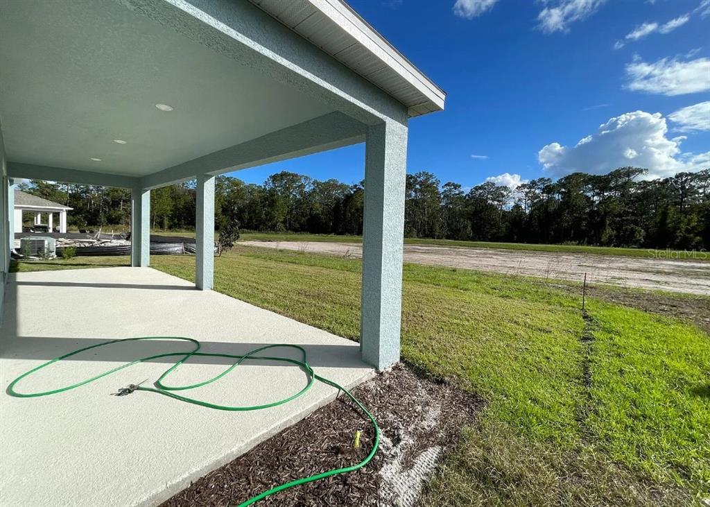 A covered concrete patio overlooks a large, grassy backyard with a line of trees — 6342 LAKEPINE STREET, ST CLOUD, FL