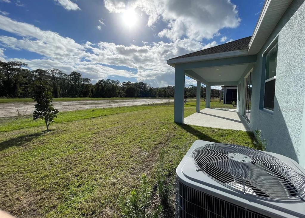 A backyard view showing a covered patio, an air conditioning unit, and a grassy lawn — 6342 LAKEPINE STREET, ST CLOUD, FL