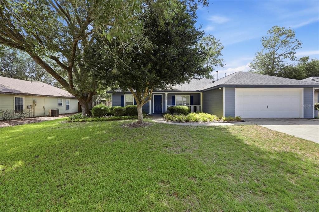 A single-story house with blue siding, a white garage door, and a large front tree — 6828 SW 82ND TERRACE, GAINESVILLE, FL