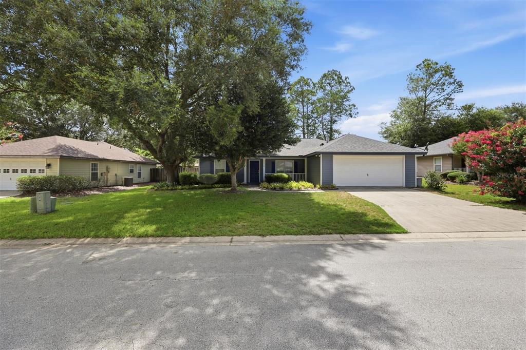 A single-story house with a white garage, blue front door, and large trees in front — 6828 SW 82ND TERRACE, GAINESVILLE, FL