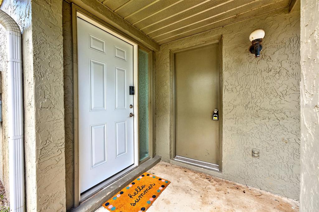 A white front door and a tan utility door sit on a covered concrete porch — 4607 RING NECK ROAD UNIT 36C, ORLANDO, FL