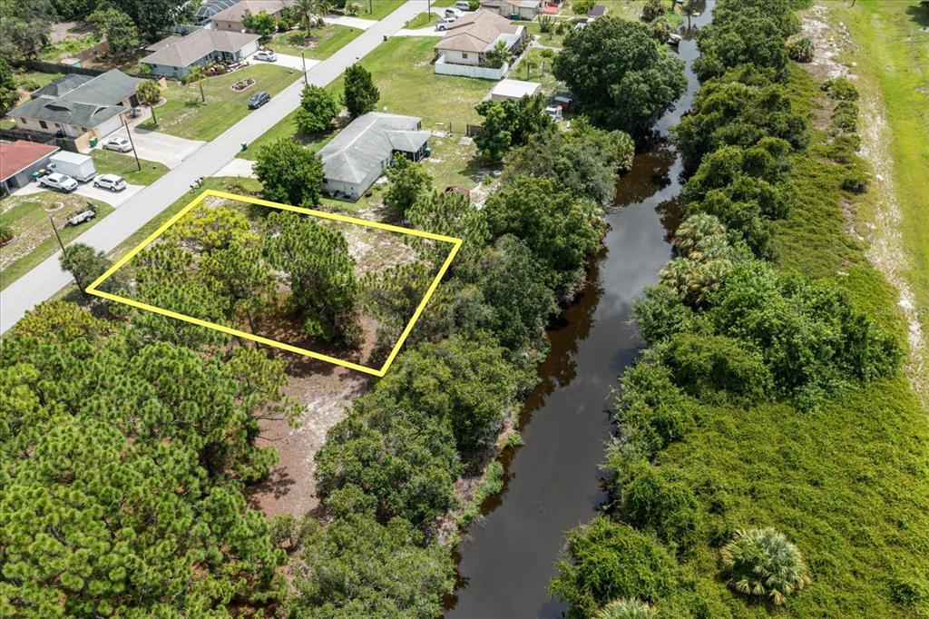 An aerial view shows a vacant, tree-covered residential lot outlined in yellow next to a canal — 10485 GREENWAY AVENUE, ENGLEWOOD, FL