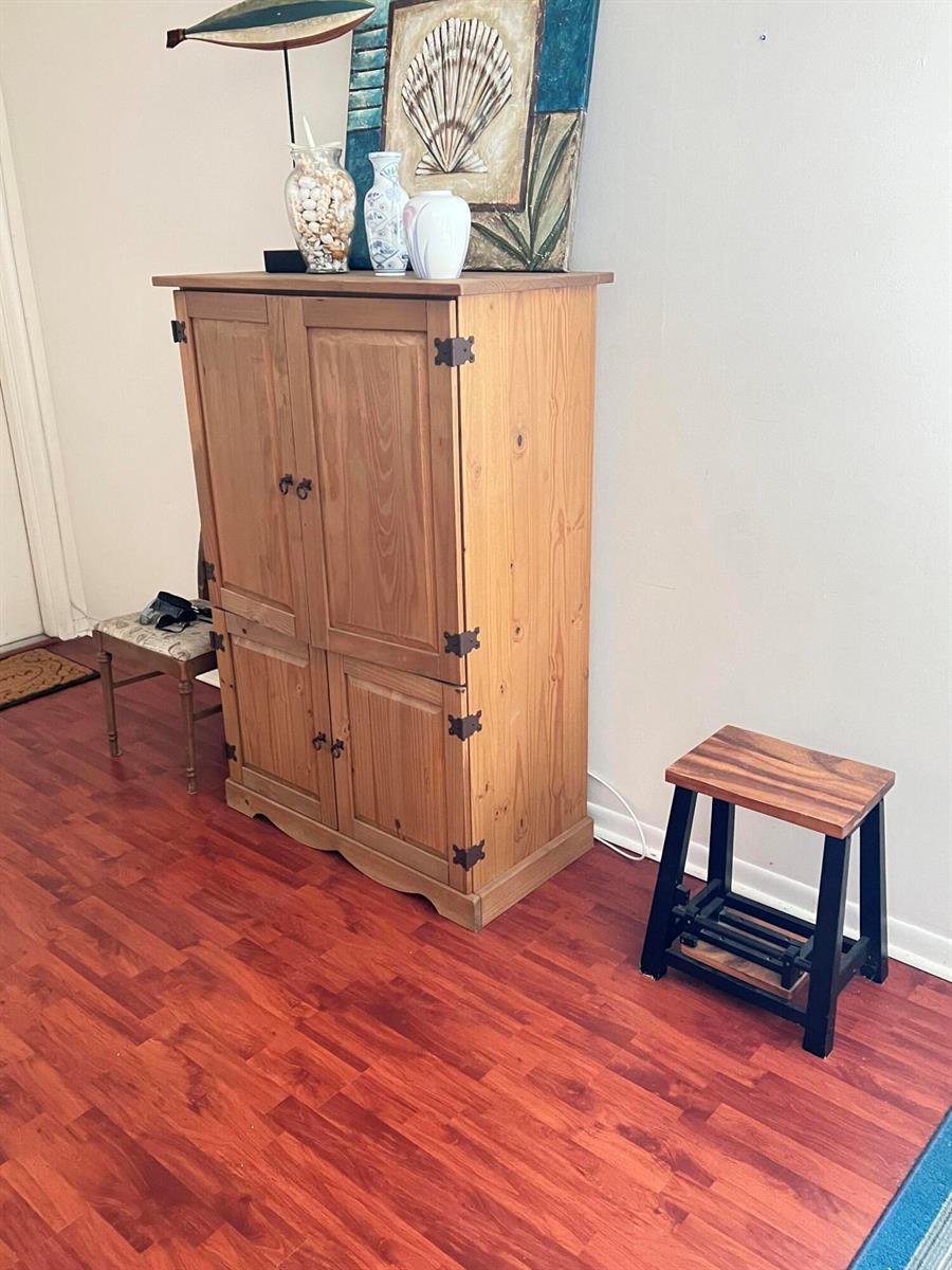 A wooden cabinet stands on a wood-look floor next to a small stool — 165 Easthampton G, West Palm Beach FL 33417, WEST PALM BEACH, FL