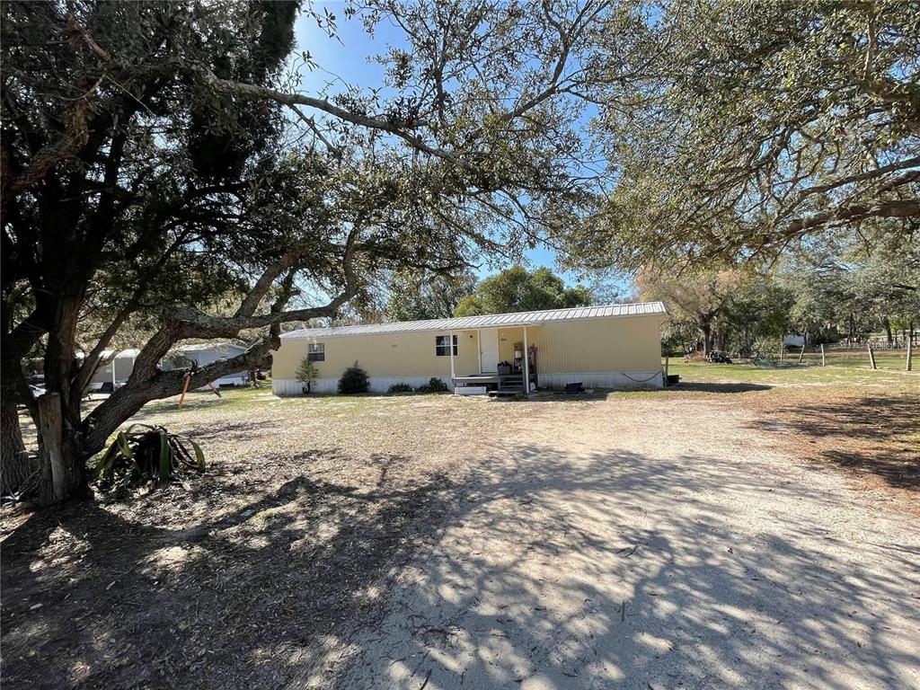 A single-story manufactured home sits on a sandy lot surrounded by large oak trees — 4385 DIETZ ROAD, BARTOW, FL
