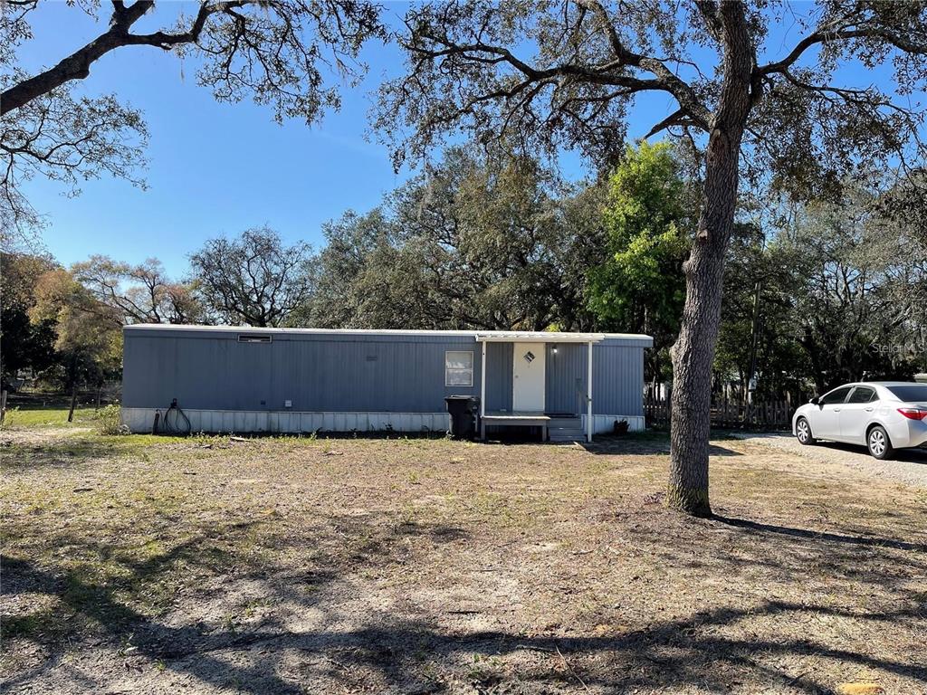 A single-story mobile home with gray siding sits on a dirt lot under trees — 4385 DIETZ ROAD, BARTOW, FL