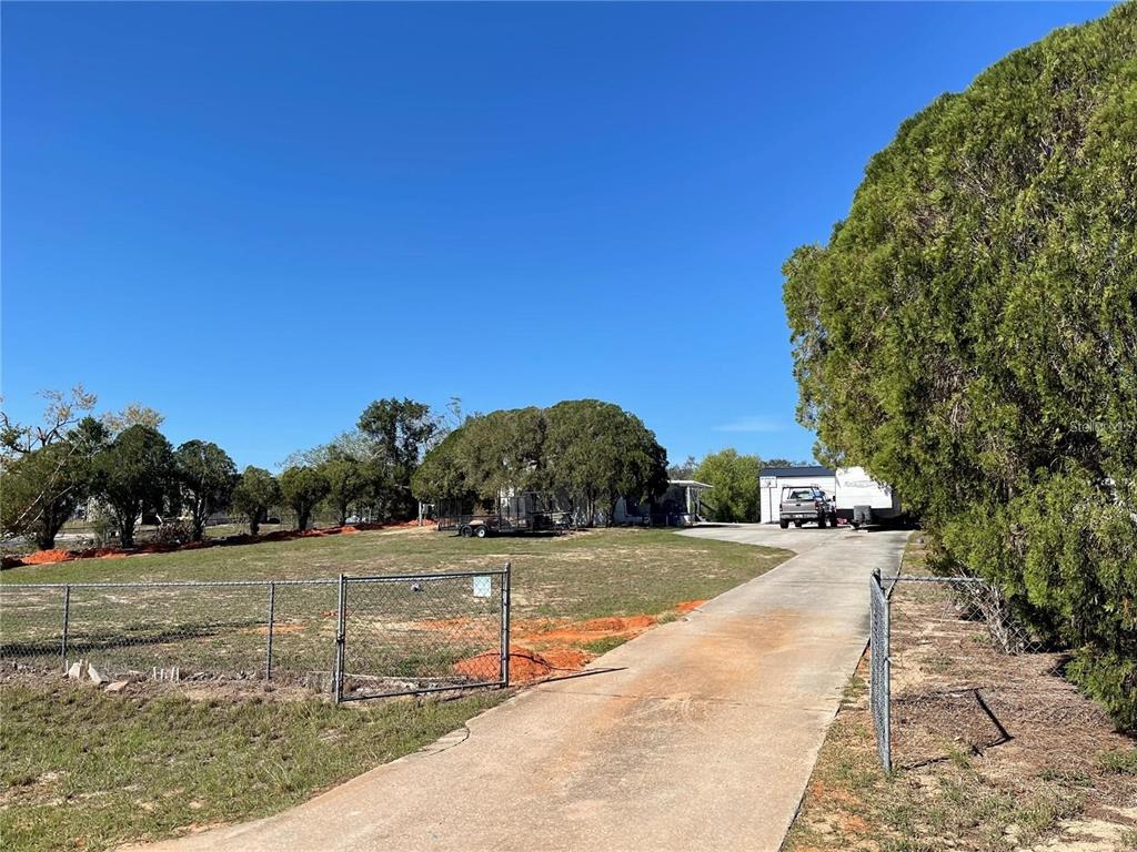 A concrete driveway leads toward a house partially obscured by trees behind a chain-link fence — 4385 DIETZ ROAD, BARTOW, FL