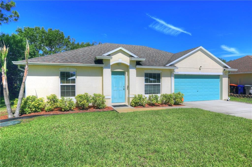 A single-story house with a light-colored stucco exterior, a teal front door, and a garage — VERO BEACH, FL