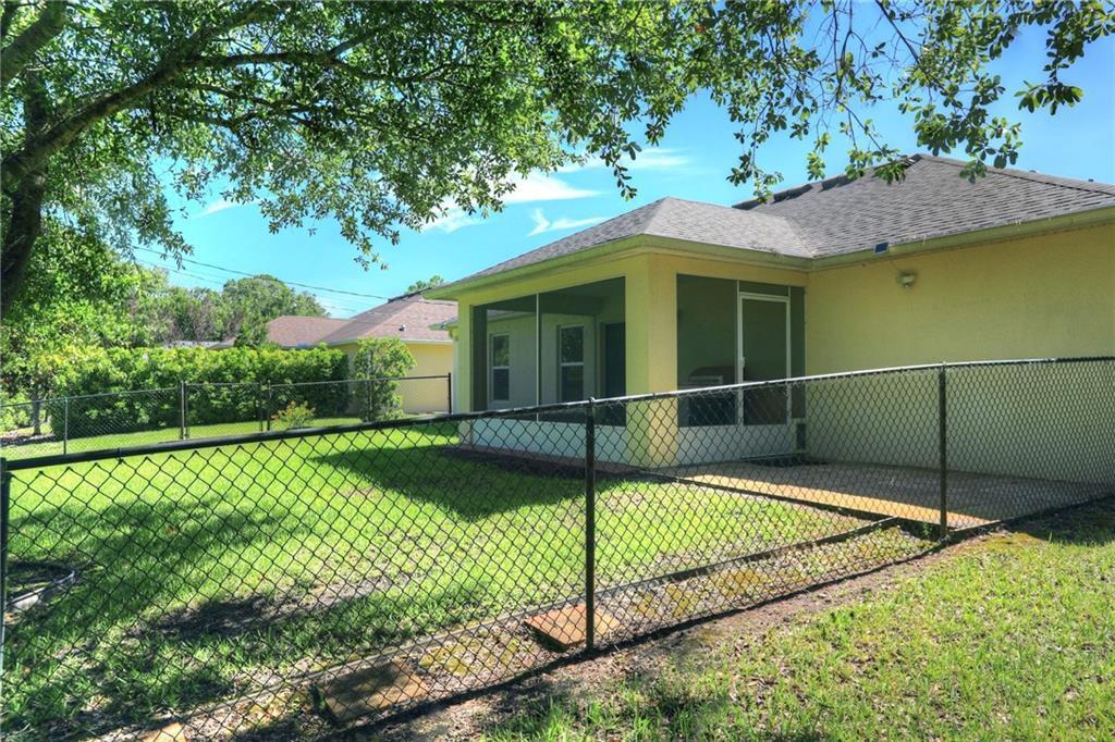 A backyard with a chain-link fence, a screened-in porch, and a yellow house exterior — VERO BEACH, FL