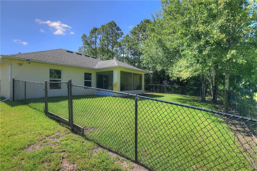 A backyard with a chain-link fence, a screened-in porch, and mature trees — VERO BEACH, FL