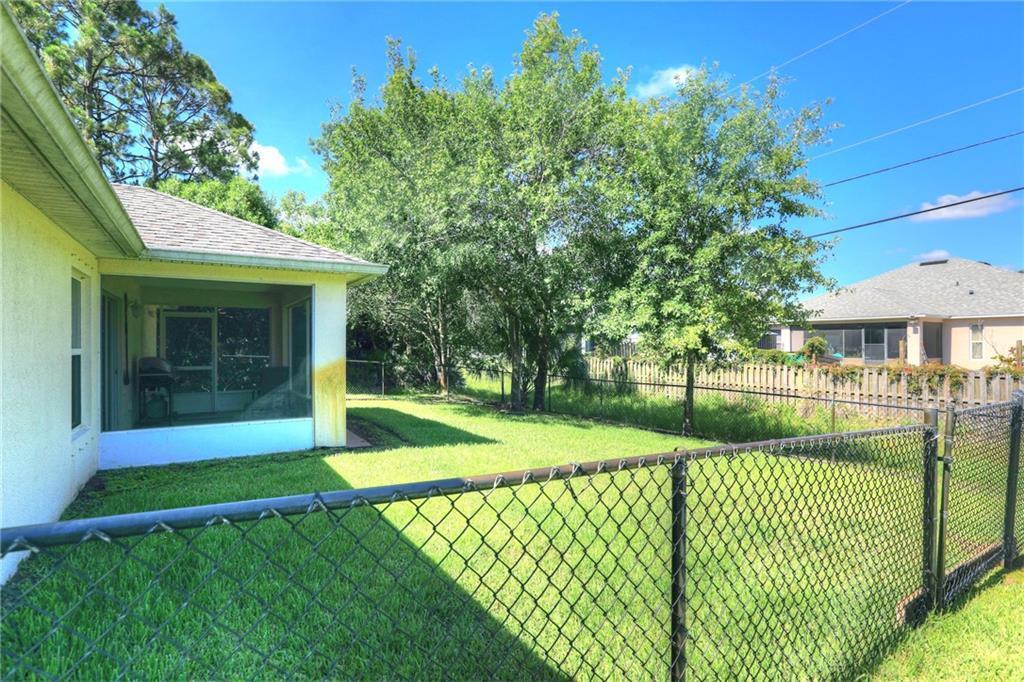 A backyard features a screened-in patio, a chain-link fence, and several mature green trees — VERO BEACH, FL