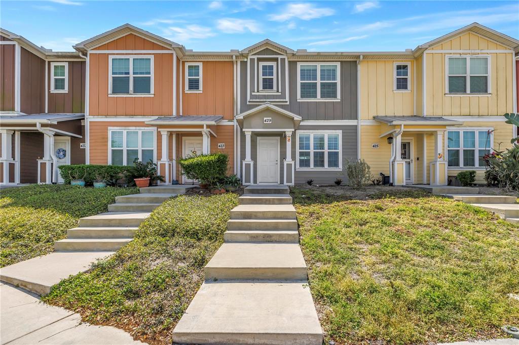 A row of three-story townhouses features colorful vertical siding and concrete walkways leading to entrances — 429 LORRAINE LELAND STREET, DUNEDIN, FL