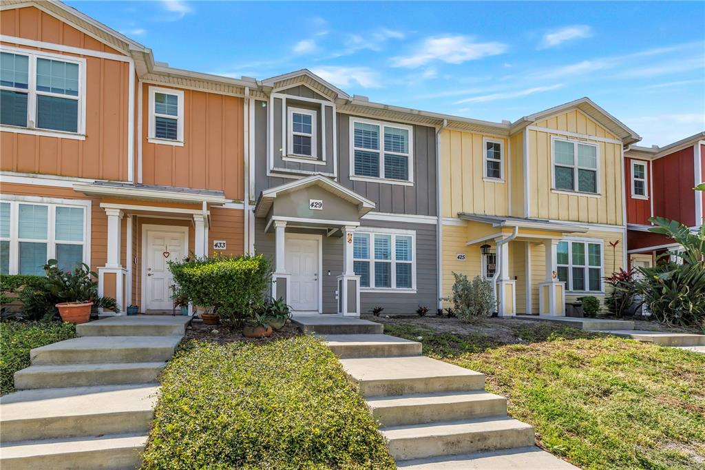 A row of multi-story townhomes with colorful siding, covered entryways, and concrete stairs — 429 LORRAINE LELAND STREET, DUNEDIN, FL